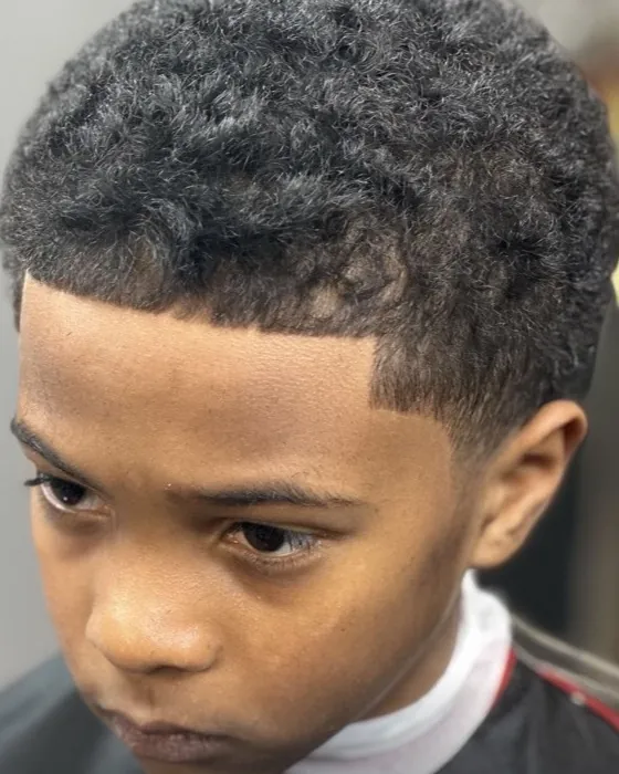 Curly top with a taper and lineup on a young client by Clifton Bey at Al-Hakeem's Tonsorial